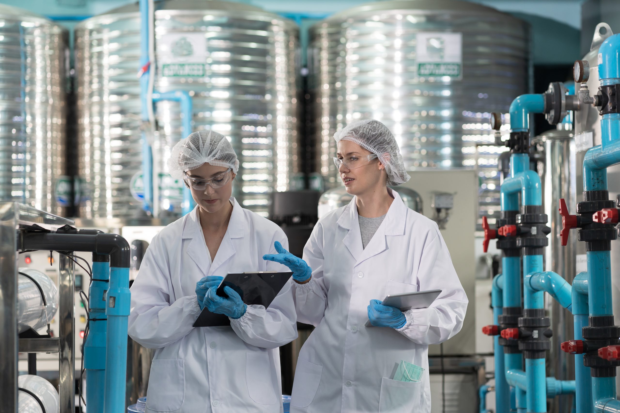 Two female worker wearing uniform, hairnet working and checking of water pump system, pipes station, Water pressure system, water tank at production line in industry factory