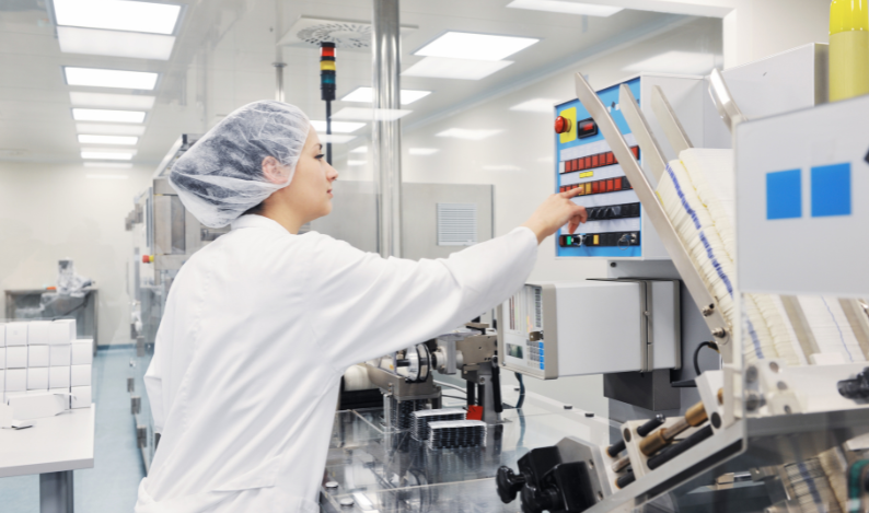 A woman in a lab coat and hair covering touching a screen.